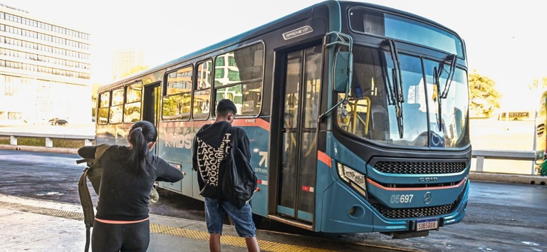 IMAGEM DE ONIBUS NA RODOVIARIA COM DUAS PESSOAS ESPERANDO EM PÉ — Agência Nacional de Transportes Terrestres